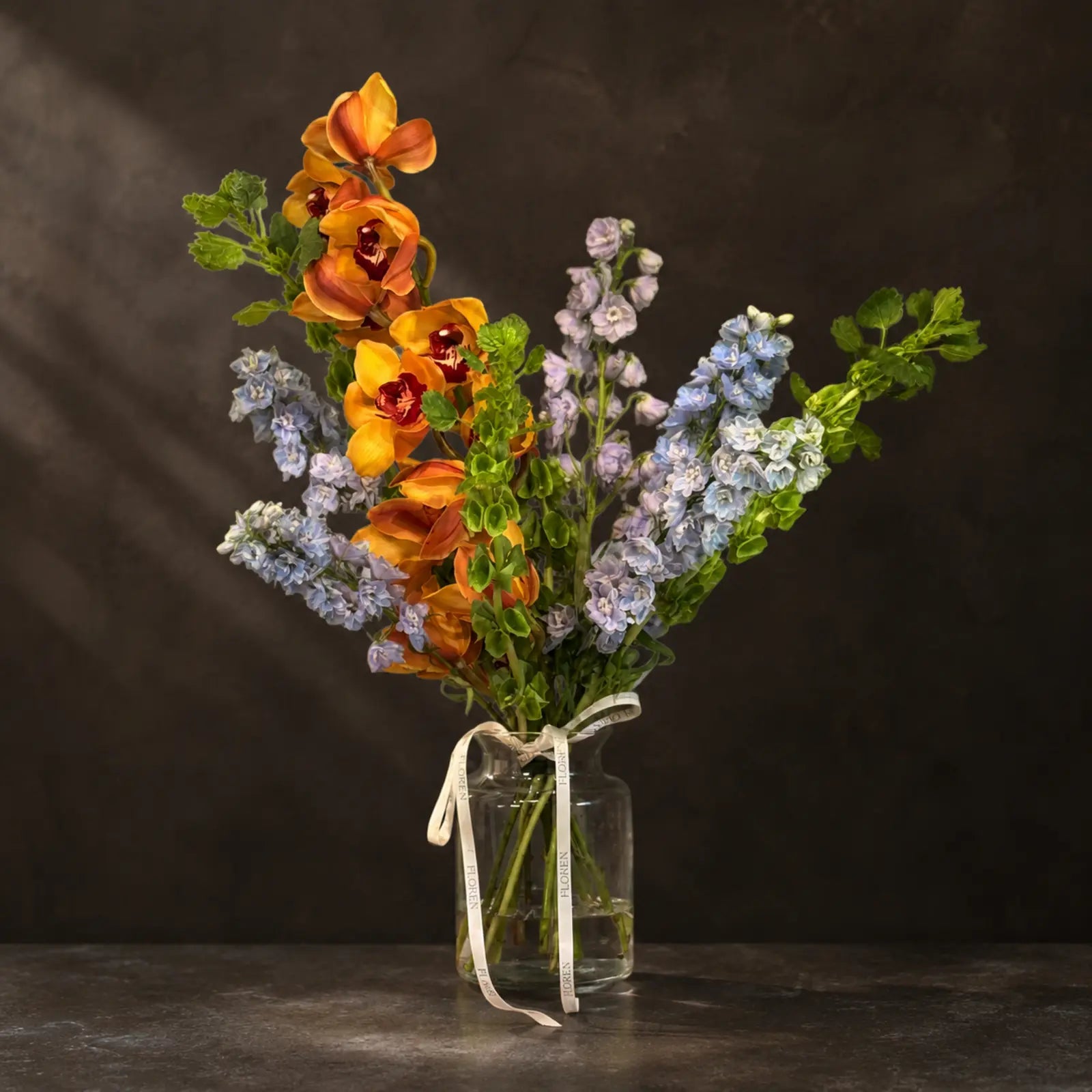 Amber Sky – blomsterarrangement med orange orkidéer og lyseblå ridderspore